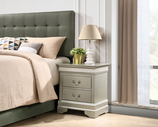 A neatly made bed with neutral bedding sits beside the Louis Phillipe Nightstand, a gray wooden piece with two drawers, topped with a beige lamp and small potted plant. Beige curtains frame the window in the background.