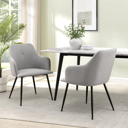 Two Contemporary Upholstered Woven Dining Chairs with black legs are placed at a rectangular white table in a bright room featuring a large window, potted plant, wall art, and a neutral rug.