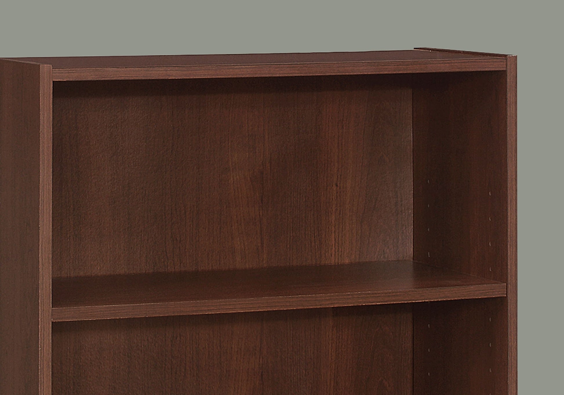 A close-up of an empty, dark brown, 4-tier transitional bookshelf for office use is set against a plain gray background.