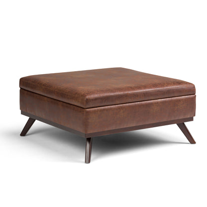 The Owen is a multifunctional square coffee table storage ottoman with mid-century modern design, featuring brown leather upholstery and angled dark wooden legs.