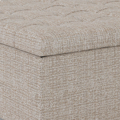 Close-up of the corner of the Harrison - Upholstered Coffee Table Storage Ottoman, featuring a beige and brown textured finish with a tufted, cushioned top and square, upholstered base.
