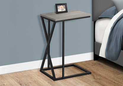 The Accent Table C - Shaped, Contemporary & Modern with a gray wood top and black metal frame sits by a bed, topped with a framed dog photo. The room features wood flooring and blue-gray walls.