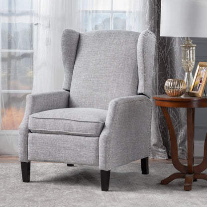 The Westeros Wing Back Fabric Upholstered Recliner in light gray sits next to a wooden side table with decor, set in a room featuring sheer curtains and large windows.