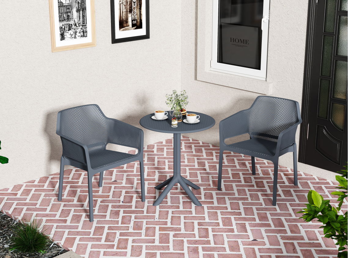 Two gray 3 Piece Plastic Arm Chair Bistro Grs Premium Ocean Plastic chairs and a round table with decor sit on a brick patio outside a beige house, with framed pictures, a window, and a door visible in the background.