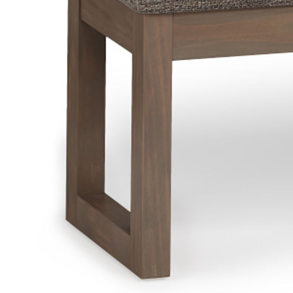Close-up of the Milltown - Upholstered Ottoman Bench featuring a wooden, rectangular open-frame leg and a brown textured seat cushion, set against a plain white background.