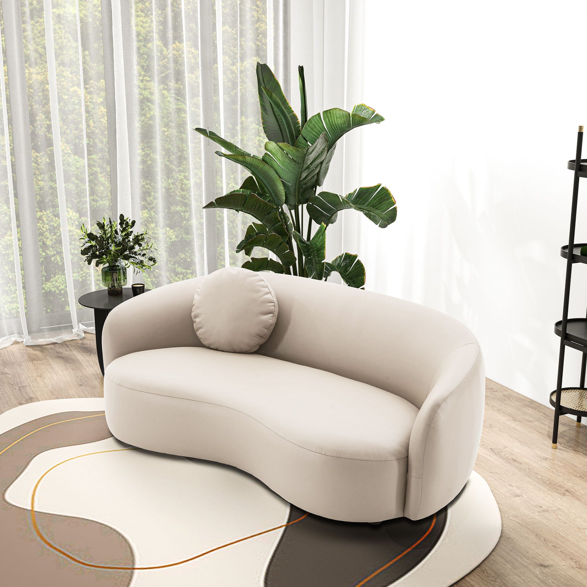 The Porter - Comfortable Sofa, featuring a modern curved beige design and round cushion, sits on an abstract rug. Behind are large green plants, a black side table with a vase, and sheer curtains framing a window with a tree view.