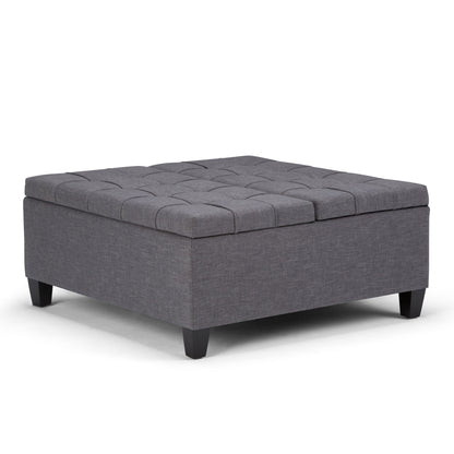 The Harrison Upholstered Coffee Table Storage Ottoman features a square design in dark gray fabric with tufted top details and short black legs, shown against a plain white background.