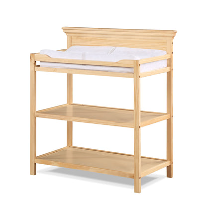 The Universal - Changing Table features a natural wood finish, classic design, two open shelves for storage, and a cushioned changing pad on top—perfect for stylish and convenient diaper changes.