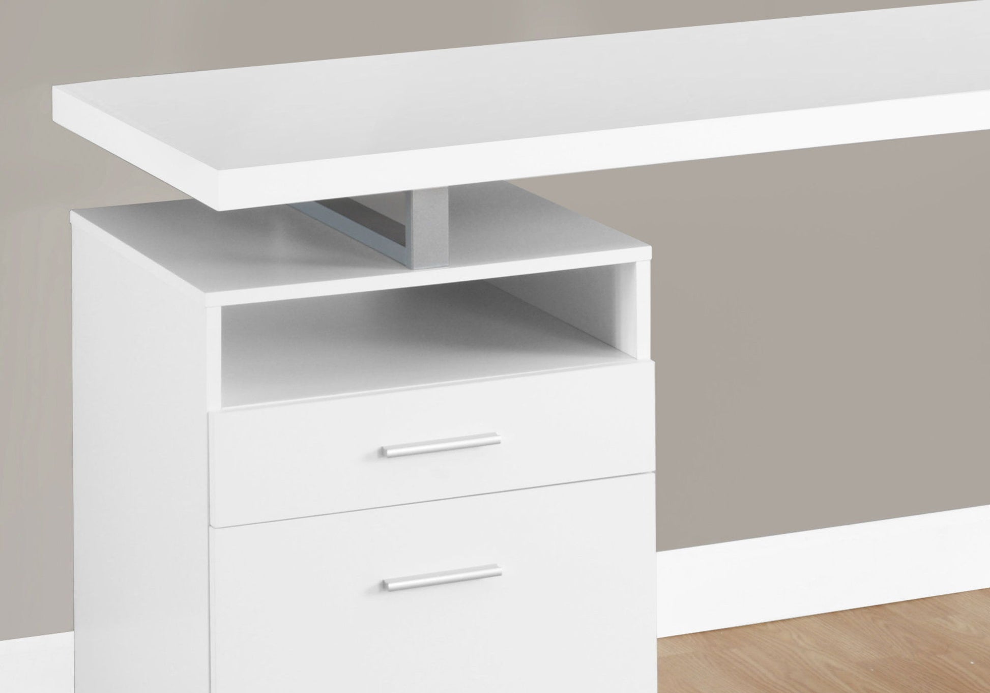 A close-up of the Computer Desk For Home Office featuring a floating tabletop, open shelf, and two drawers with silver handles. The contemporary white desk stands on a light wood floor with a light gray-beige wall behind it.