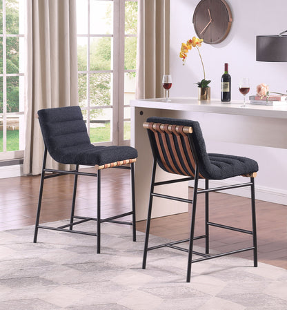 Two Lahni 17" Boucle Fabric Counter Height Chairs with black seats and wooden backs stand at a white counter in a bright room featuring large windows, curtains, a wall clock, wine glasses, a wine bottle, and a plant.