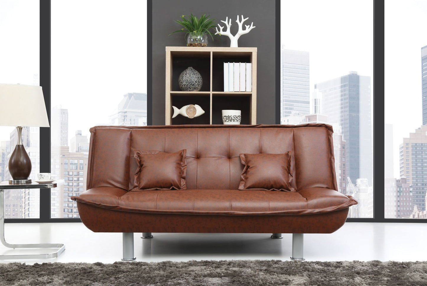 A modern living room featuring the Lionel - Sofa Bed in brown leather with two matching pillows, a shaggy rug, a contemporary lamp, and a wooden shelf decorated with plants. Large windows showcase a city skyline.