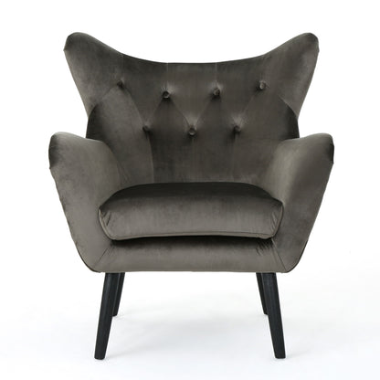 The Alyssa Mid Century Upholstered Arm Chair features a dark gray velvet finish, wingback design, button tufting, and angled black wooden legs, shown against a white background.