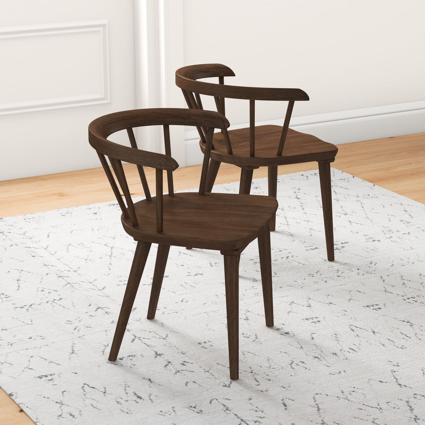 Two Kingsley Dining Chairs (Set of 2, Brown) with curved backrests and spindled supports sit on a light patterned rug in a bright room featuring light wood flooring and white walls.