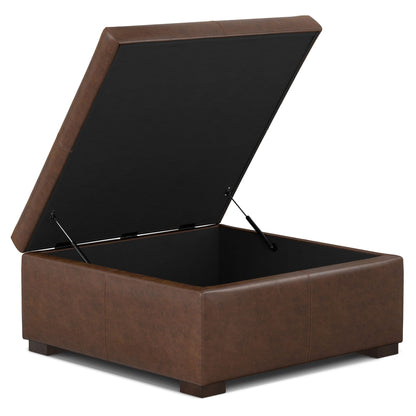 The Gabbie Coffee Table Upholstered Storage Ottoman is a brown, square leather piece with a hinged lid that opens to reveal storage space inside, resting on short, sturdy legs.