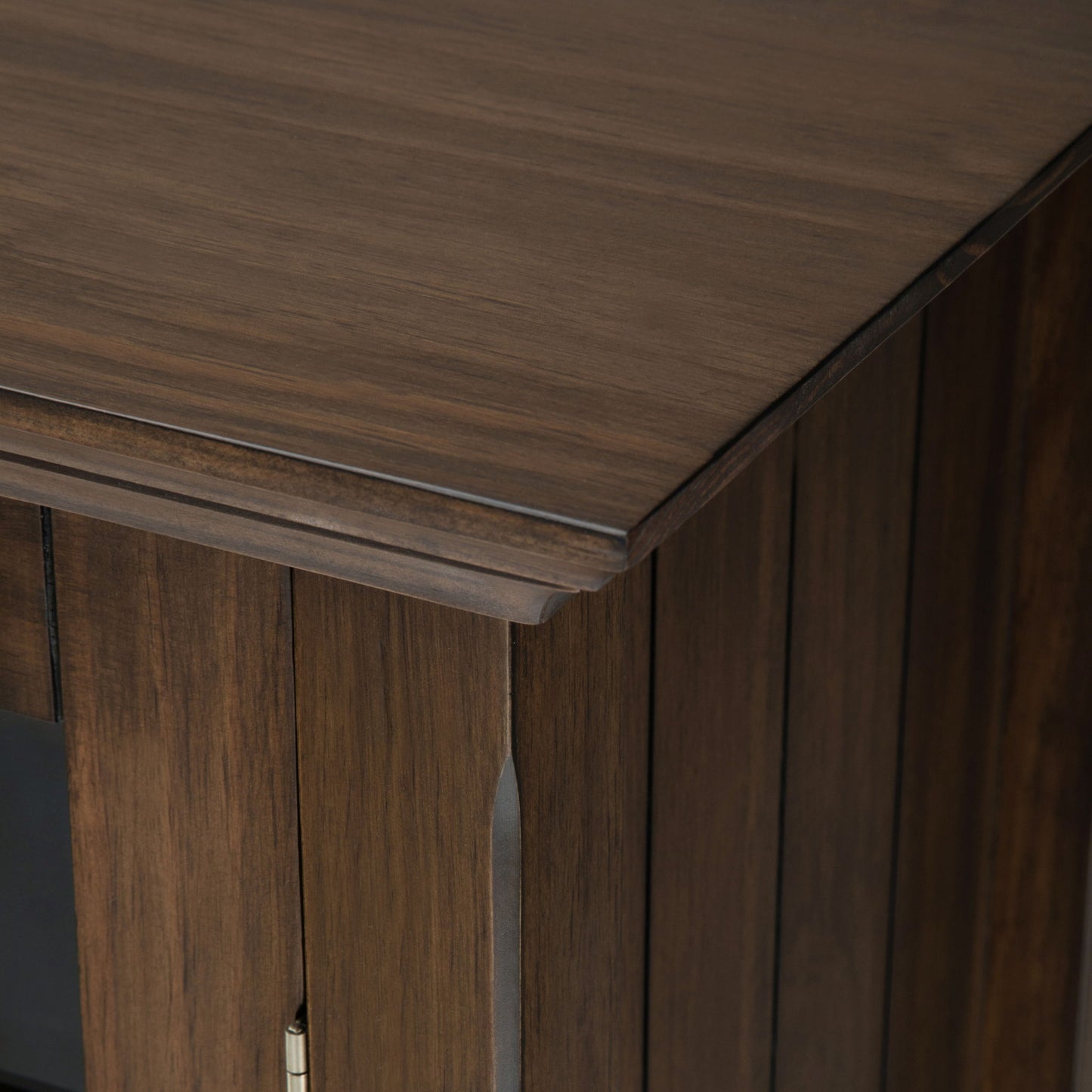 Close-up of the top and corner of the Bedford - Storage Media Cabinet, featuring its dark brown finish, visible wood grain, and detailed panel design.
