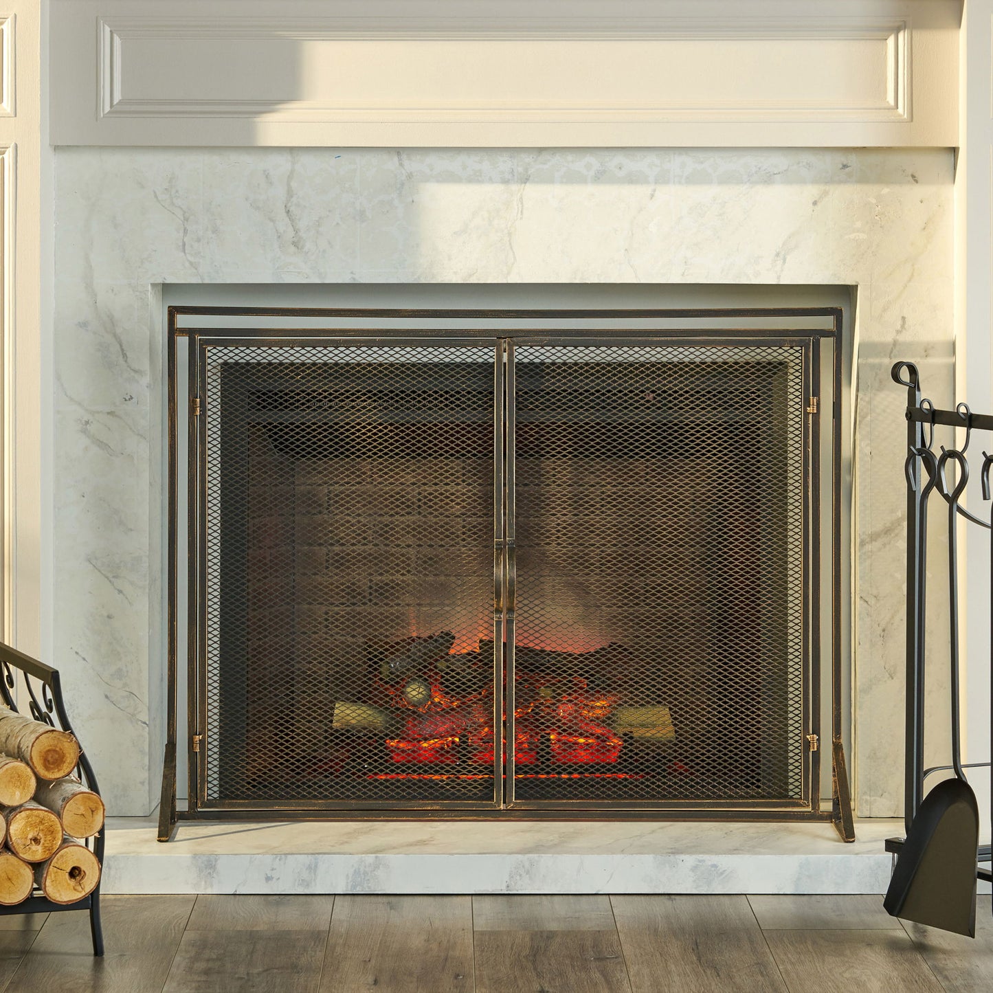 A marble fireplace with the Samantha Iron Fireplace Screen (2-Door Design), glowing logs inside, and a set of firewood and fireplace tools beside it on a wooden floor.