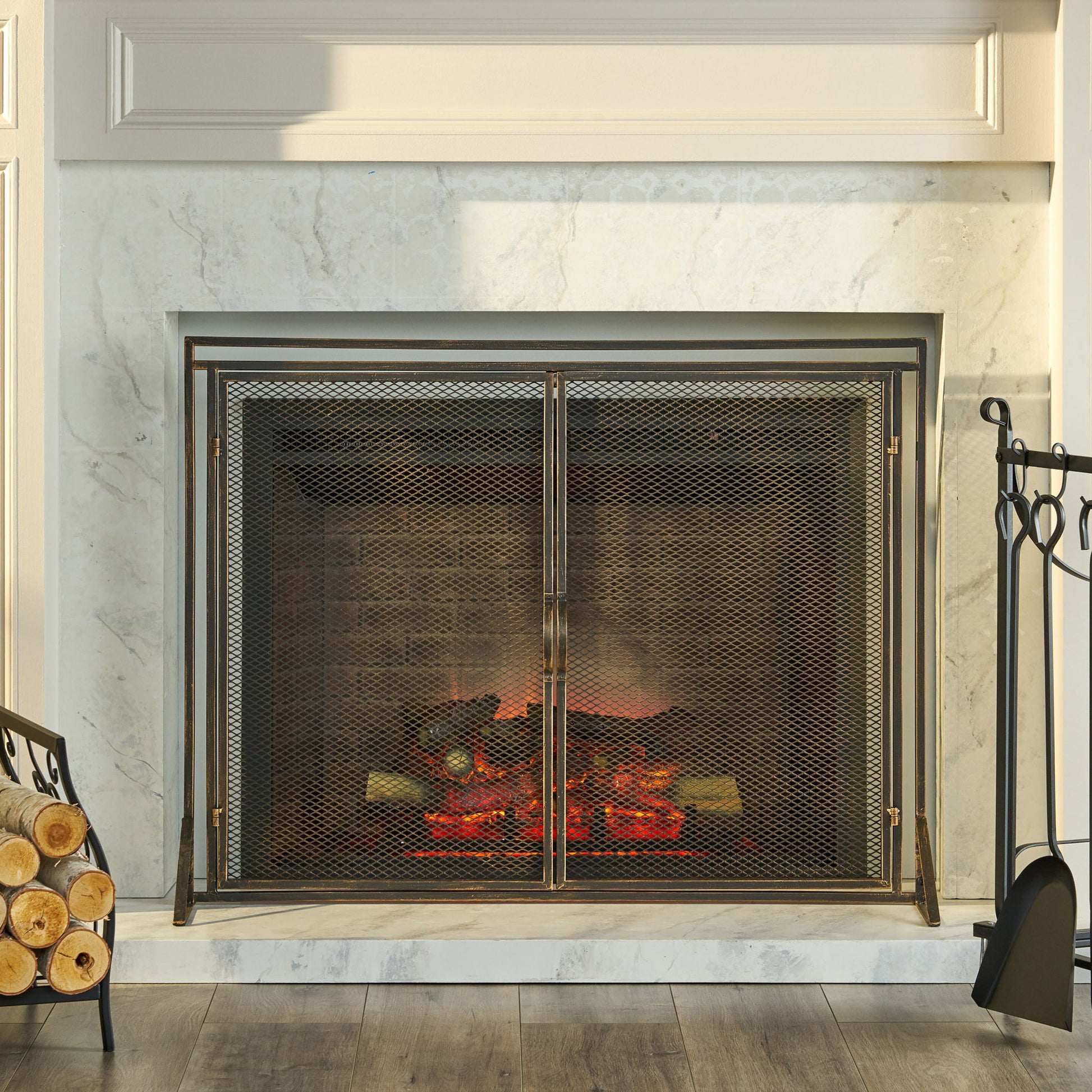 A marble fireplace with the Samantha Iron Fireplace Screen (2-Door Design), glowing logs inside, and a set of firewood and fireplace tools beside it on a wooden floor.