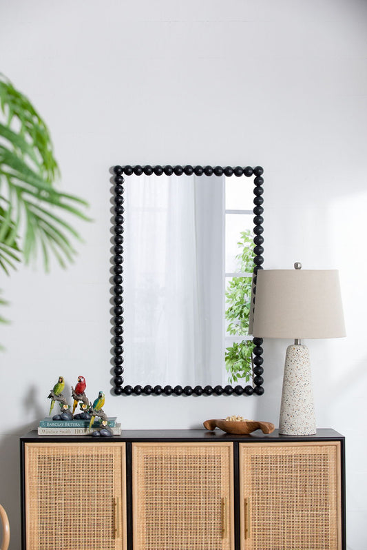 A decorative cabinet displays bird figurines, books, a bowl, and a speckled lamp; above it hangs the Rectangle Mirror, Wall Mirror For Living Room Bedroom Entryway - Black, reflecting a window and greenery.