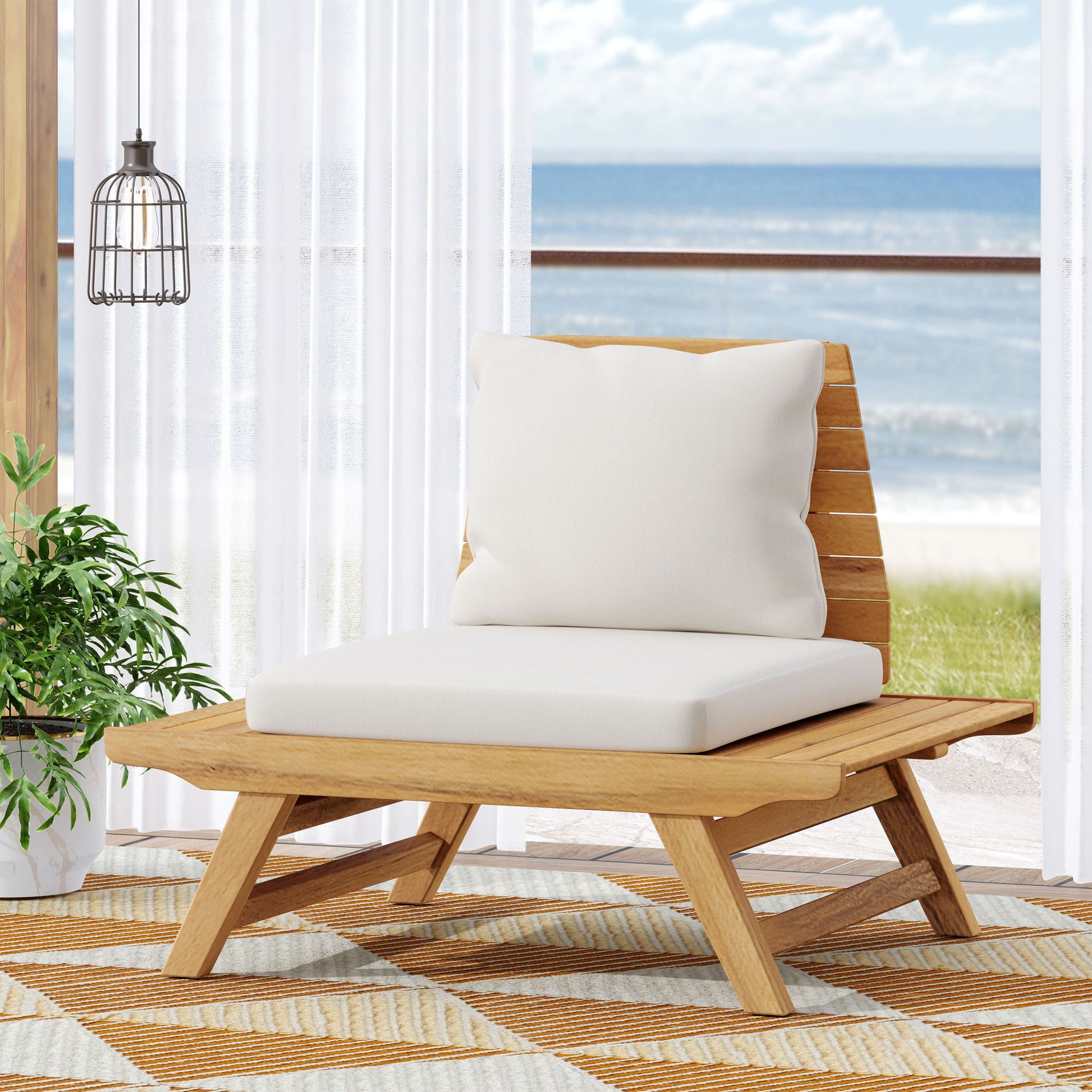 The Sedona Outdoor Club Chair with a slatted design and white cushions is placed on a patterned rug near a large window, overlooking the ocean. A potted plant and hanging light complete the modern coastal setting.