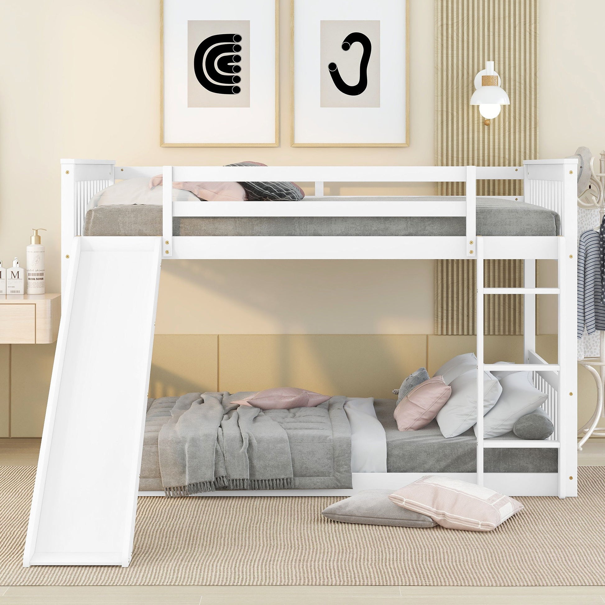 A modern kids' room with the Bunk Bed With Slide And Ladder in white. The lower bed has gray and pink bedding, the upper has gray bedding. Minimalist wall art and a reading lamp hang above a neutral-toned rug.