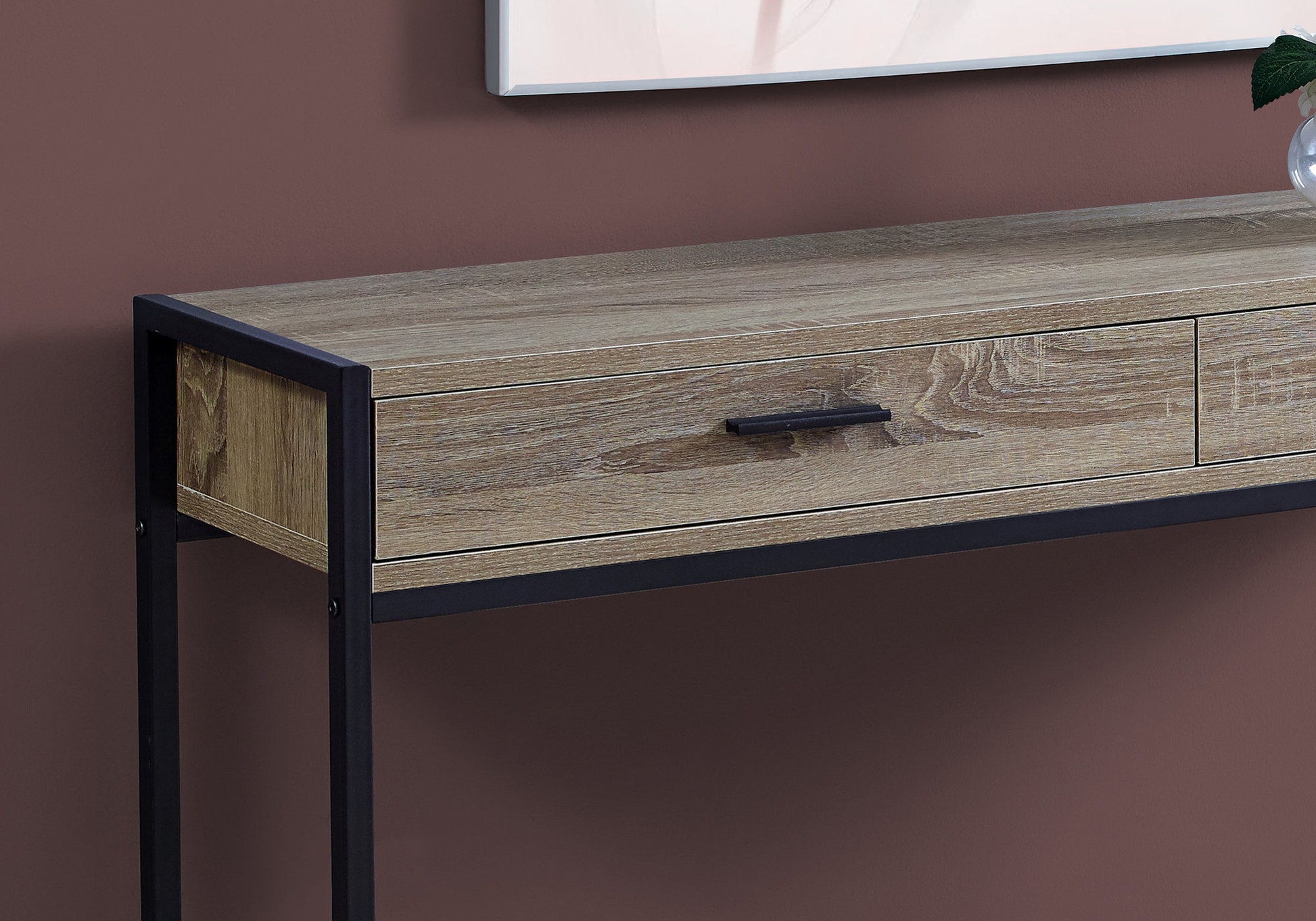 A close-up of the Accent Console Table For Entryway, featuring a light wood finish, black metal frame, single storage drawer with a black handle, shown against a mauve wall in a contemporary and modern style.