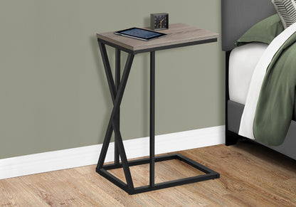 The Accent Table C - Shaped, Contemporary & Modern with a wooden top and black metal frame sits beside a bed, holding a tablet and small clock. The room features wood flooring and a green wall.
