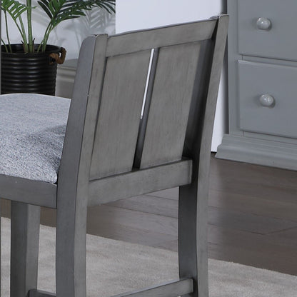 A close-up of the Graham 20" Upholstered Seat Counter Height Chair (Set of 2) in gray, featuring padded seats, placed on a light rug beside a matching gray dresser and a potted plant in the background.