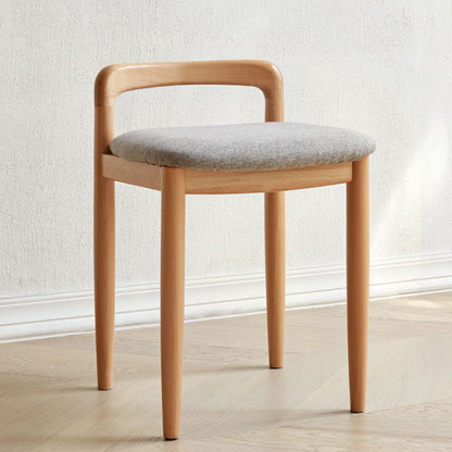 The Stool Bed For Dining Room - Natural, featuring a modern wooden design with a curved backrest and light gray cushioned seat, sits on a light wood floor against a plain white wall.