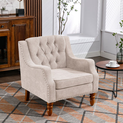 A comfy Accent Chair set with vintage brass studs and button-tufted upholstery is placed on a patterned rug by a window, near a small round table with a cup and saucer, in a bright modern room with a wooden cabinet.