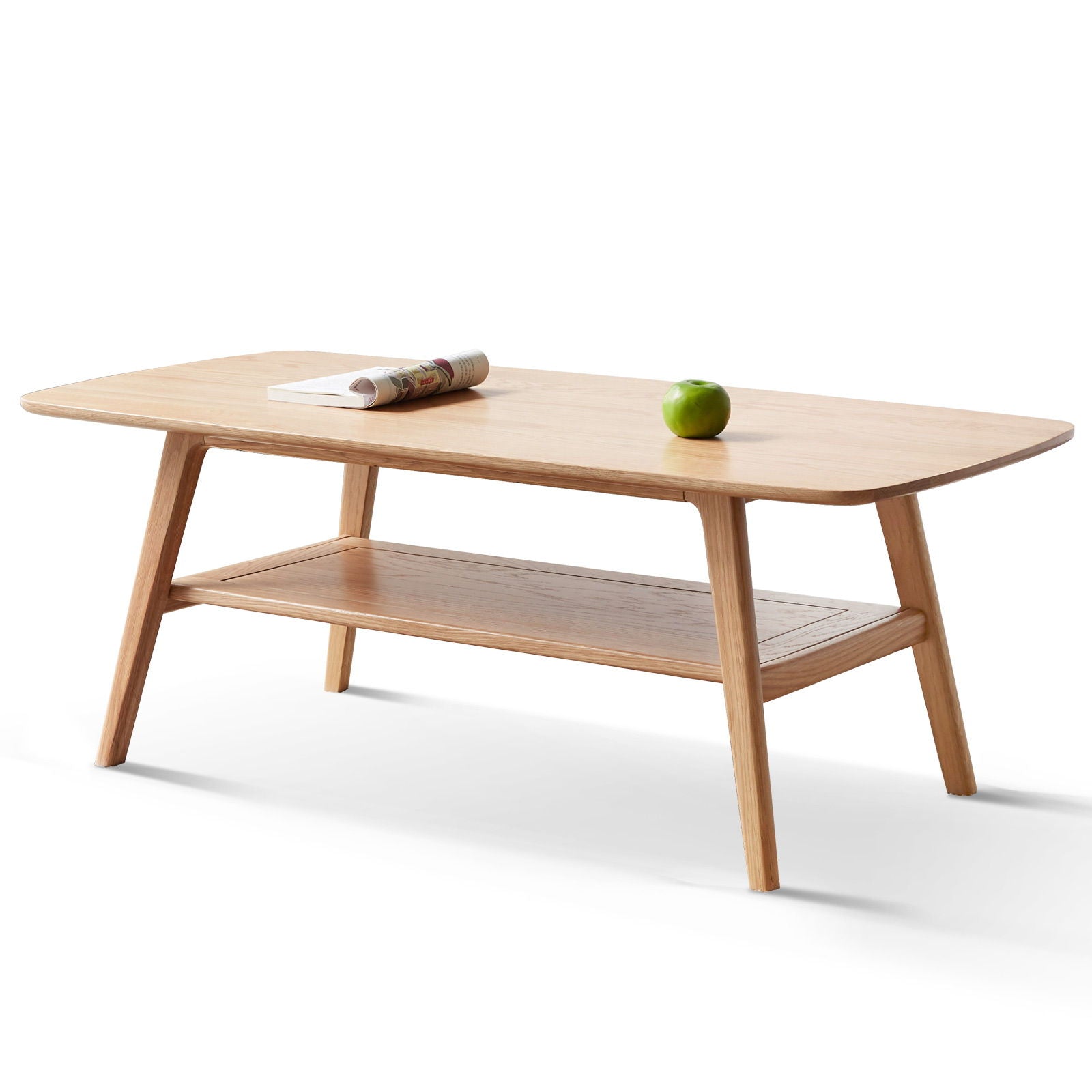 The Low Coffee Table With Storage Shelf features angled legs, a lower shelf, and rounded edges. A rolled-up magazine and a green apple are placed on top of the table.