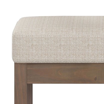 Close-up of the Milltown Upholstered Ottoman Bench featuring a cushioned seat in light beige textured fabric and a wooden frame with a rich brown finish.