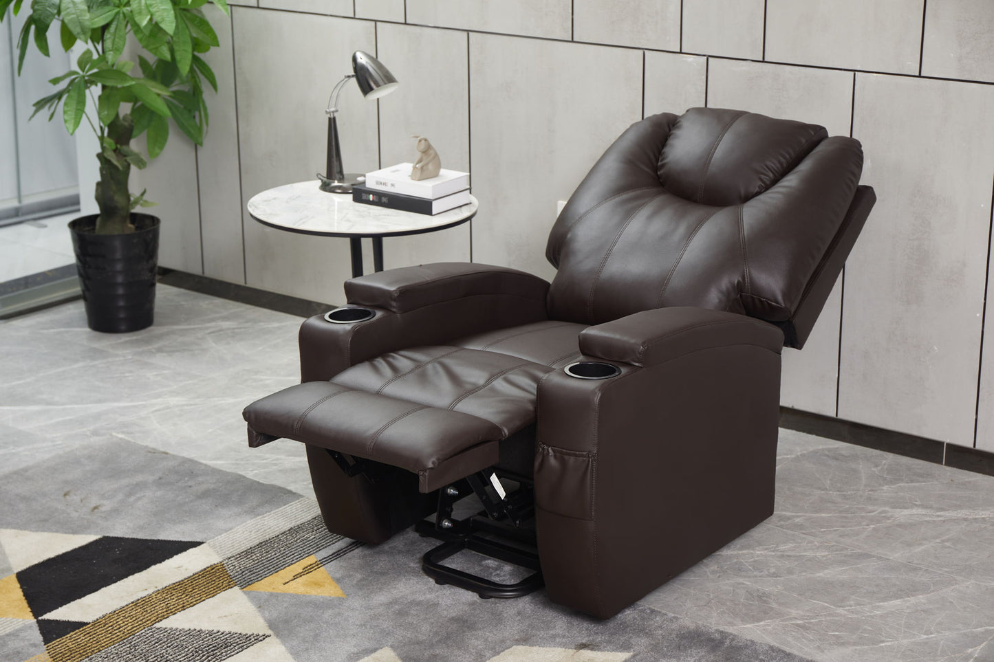 The Modern Recliner Chair With Cup Holders, Remote Control is fully extended in a modern living room beside a round side table with books, a lamp, and a small plant. A large potted plant and geometric rug complete the stylish scene.