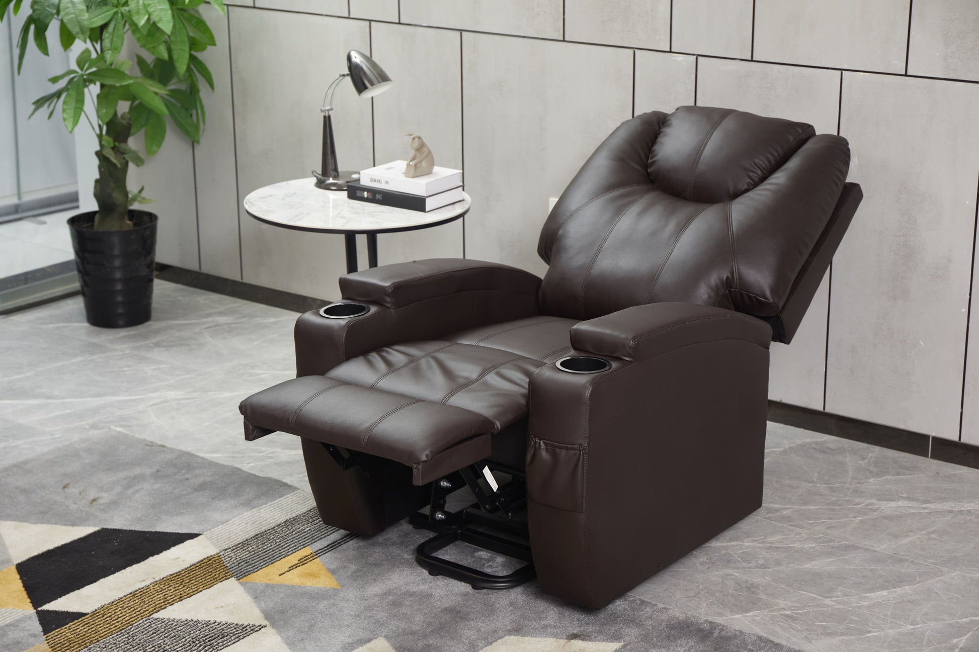The Modern Recliner Chair With Cup Holders, Remote Control is fully extended in a modern living room beside a round side table with books, a lamp, and a small plant. A large potted plant and geometric rug complete the stylish scene.