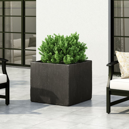 A green shrub thrives in a Modern Outdoor Planter, a large square black container set on a tiled patio, accompanied by modern outdoor chairs with light cushions. Glass doors and a white wall complete the stylish background.