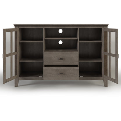 The Artisan Handcrafted Tall TV Media Stand features two glass-paneled doors, six shelves, two central drawers, and two circular cable cutouts on the back. Finished in medium brown wood grain.