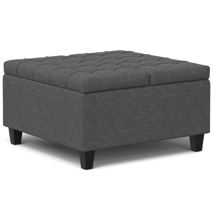 The Harrison Upholstered Coffee Table Storage Ottoman features a square, dark gray tufted top and short black legs.