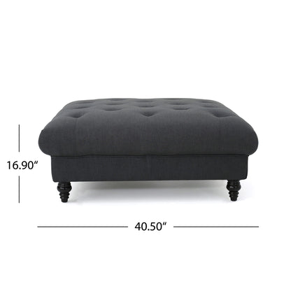 The Madrid Tufted Ottoman Footrest features a dark gray upholstered design, tufted top, wooden legs, and measures 16.9 inches tall by 40.5 inches wide.