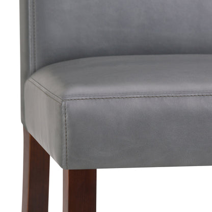 Close-up of the Acadian - Upholstered Parson Dining Chair, featuring a smooth gray upholstered seat and seatback with visible stitching, and straight dark wooden legs. Sold as a set of 2.