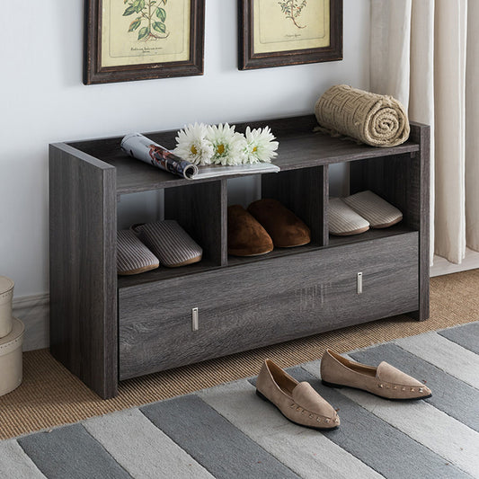 A Shoe Entry Bench With Three Shelves and a drawer holds slippers, a rolled towel, and white flowers on top. Set against a wall with framed art, it stands over a striped rug where flats rest in front.