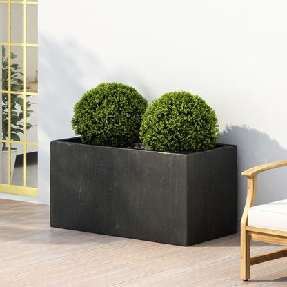 The Modern Outdoor Planter, a rectangular black box with two round green bushes, sits on a wooden deck beside a white cushioned chair and a yellow-framed glass door.