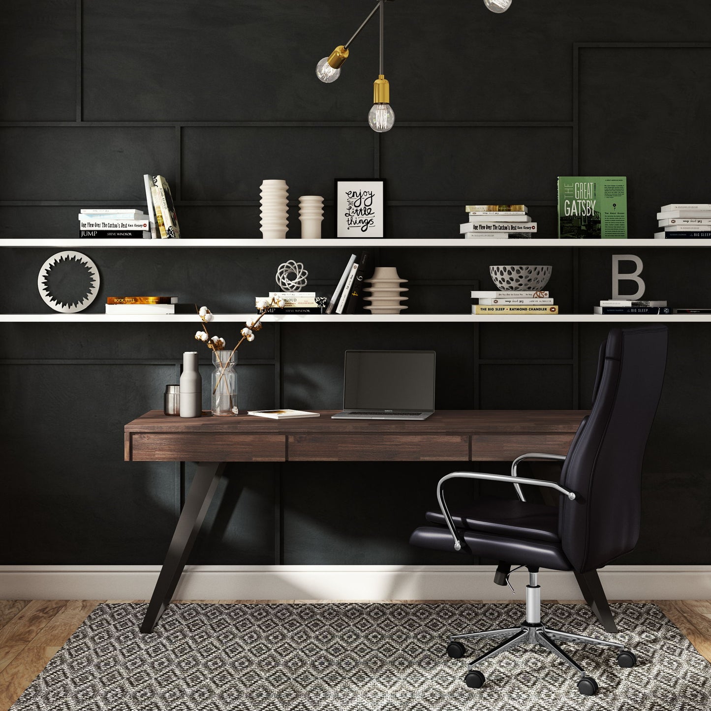 Modern home office with a dark accent wall, floating shelves holding books and decor, the Lowry - Handcrafted Desk with a closed laptop and vase of flowers, plus a black ergonomic chair on a patterned rug.