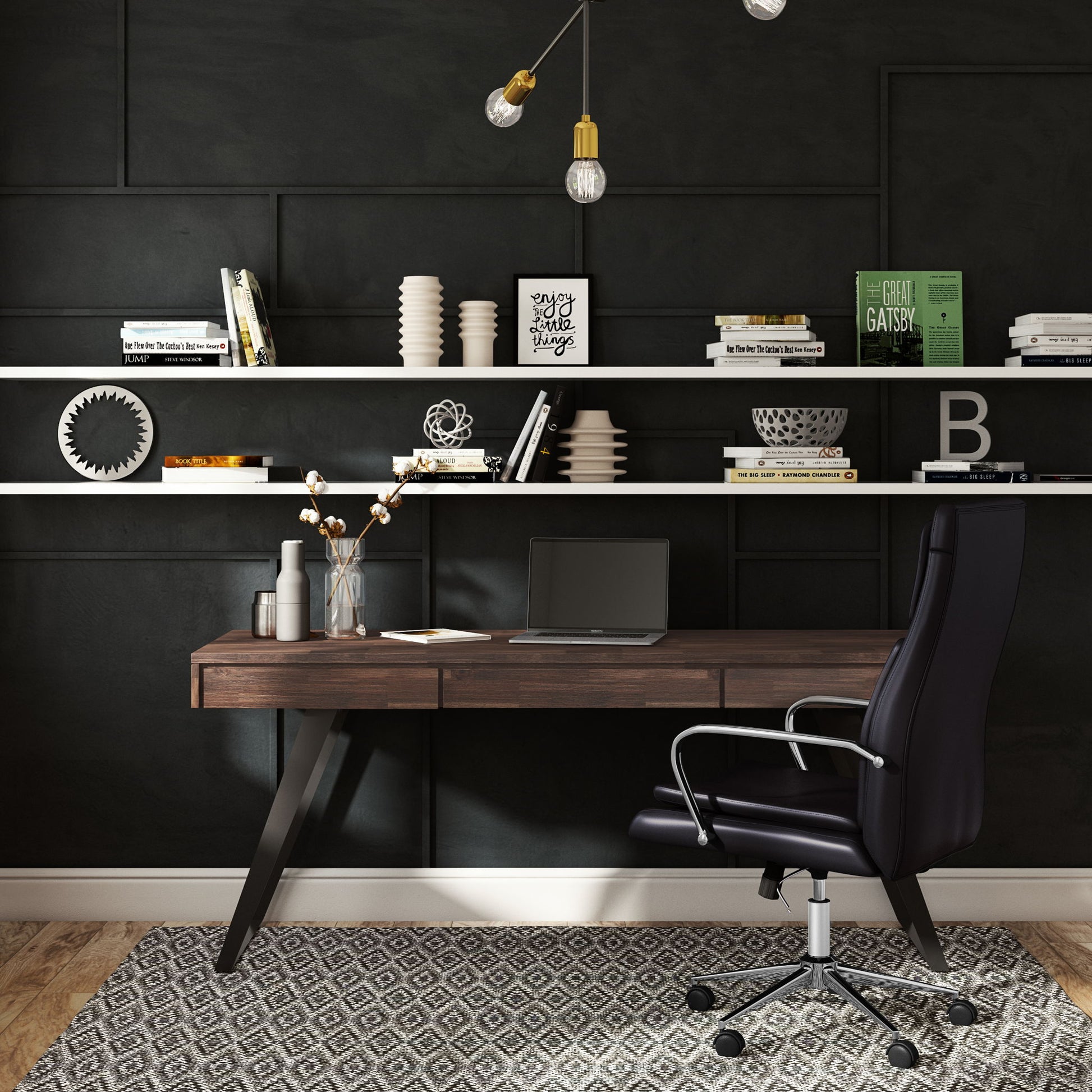 Modern home office with a dark accent wall, floating shelves holding books and decor, the Lowry - Handcrafted Desk with a closed laptop and vase of flowers, plus a black ergonomic chair on a patterned rug.