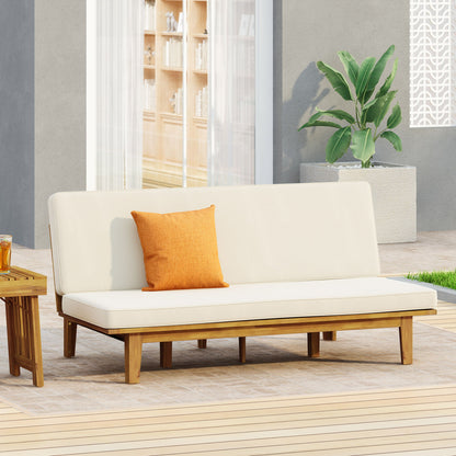 The Outdoor Elegance Daybed With Convertible Design Cushion Frame - Beige is set on a patio, featuring soft beige cushions and an orange pillow beside a small drink table, with a large potted green plant and glass doors in the background.