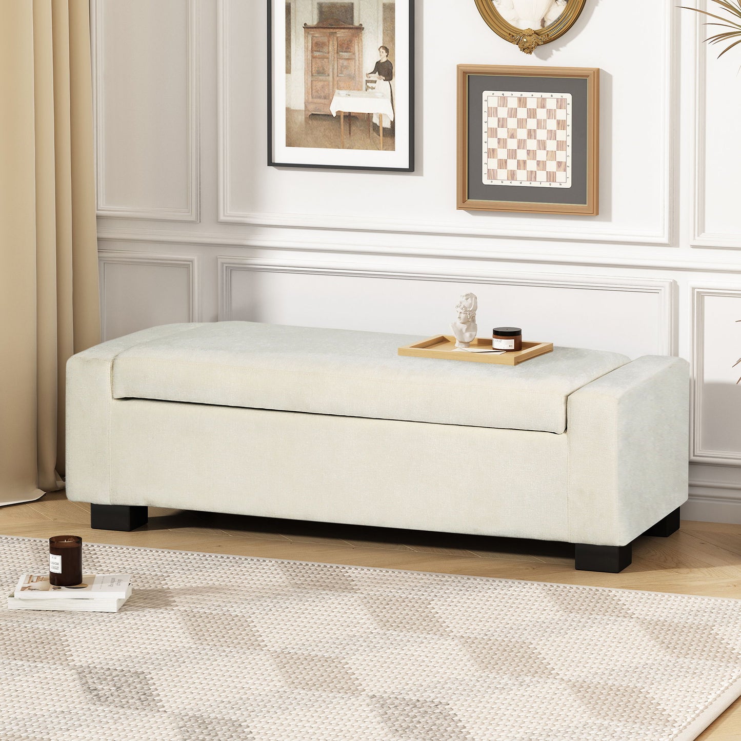A Textured Fabric Ottoman Bench With Hinged Lid sits against a white paneled wall with framed art. A wooden tray with decor and candles is on the bench, while a patterned rug covers the floor.