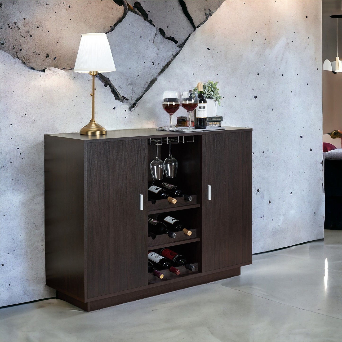 The Hazen - Wine Cabinet II - Espresso displays wine bottles and glasses, topped with a table lamp and wine setup, all set against a striking modern concrete wall with a bold cracked design.