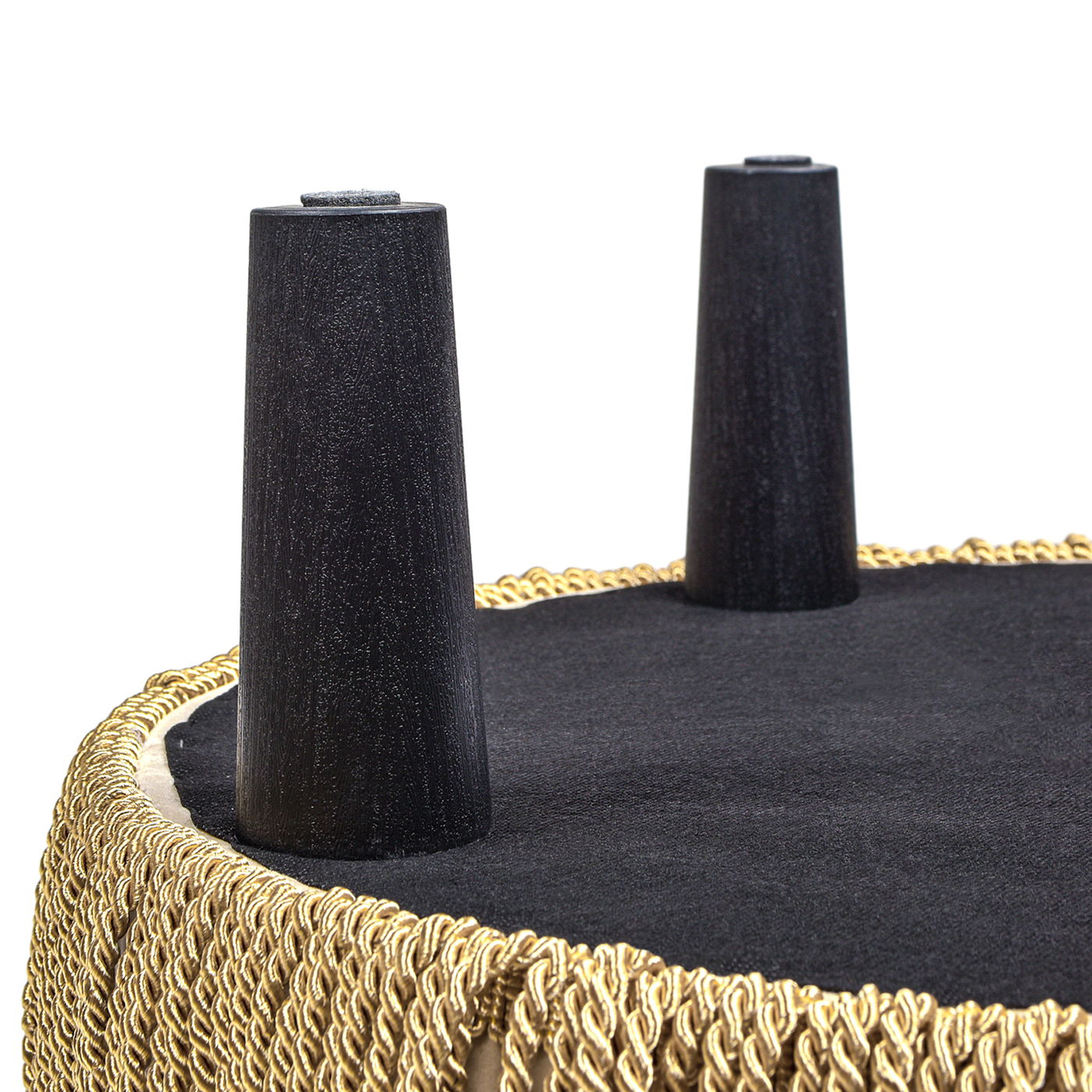 Close-up view of the underside of the Yolanda - Round Upholstered Accent Ottoman, featuring two black cone-shaped legs and a decorative gold fringe around the edge.
