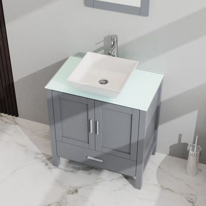 The Bathroom Vanity And Sink Combo Glass Top Cabinet With Mirror features a modern gray finish, double doors, white square vessel sink on frosted glass countertop, chrome faucet, and sits on a white marble floor with a small cylindrical trash bin.