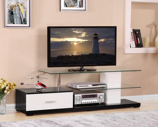 The Ivana TV Stand in White/Black holds a flat-screen TV showing a sunset lighthouse. Glass shelves display a stereo receiver, DVD player, remote helicopter, and books. Nearby are a flower vase and framed art.