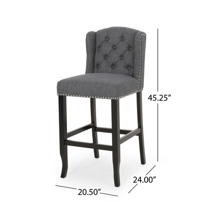 The Vienna Contemporary Fabric Tufted Wingback Counter Stools (Set of 2) feature dark gray upholstery, tufted backrest, silver nailhead trim, black wooden legs, and measure 45.25"H x 24"D x 20.5"W.
