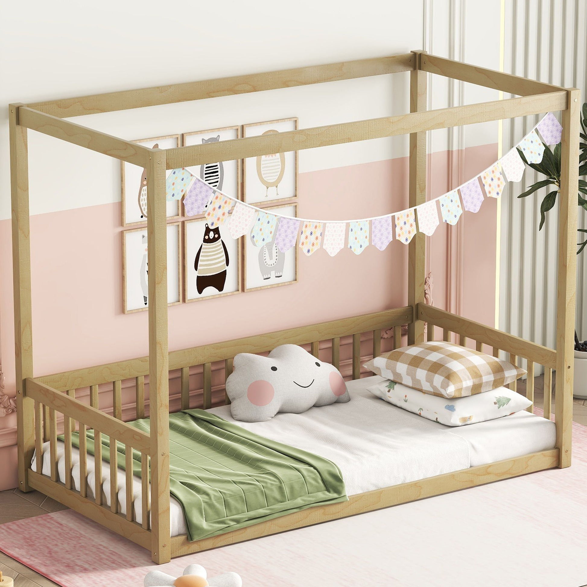 A Canopy Frame Floor Bed With Fence, Guardrails shaped like a house sits in a pastel-themed room with a green blanket, elephant and checkered pillows. Colorful buntings hang above and animal prints decorate the wall.